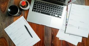 Portatile e fogli di documenti con una penna su una scrivania in legno vista dall'alto