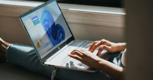 Mani che scrivono su un portatile con Windows 11 appoggiato sulle gambe