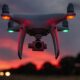 Drone quadricottero in volo al tramonto con le luci di posizione accese e il cielo rosso sullo sfondo