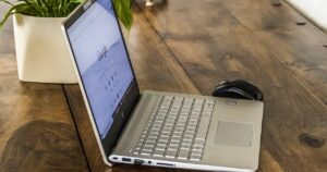 Computer portatile aperto su una scrivania in legno, accanto a un mouse e a una pianta in vaso