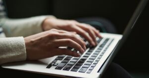 Mani che scrivono sulla tastiera di un portatile in penombra