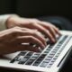 Mani che scrivono sulla tastiera di un portatile in penombra