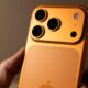 Mano che tiene un iPhone 17 Pro arancione visto da dietro, con il modulo fotografico a tre obiettivi