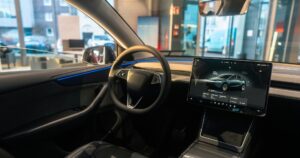 Abitacolo della nuova Tesla Model Y con il volante, la luce ambiente blu e lo schermo centrale acceso