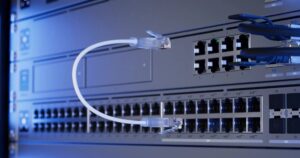 Primo piano di switch UniFi in rack con porte Ethernet e SFP e un cavo di rete bianco, in luce blu