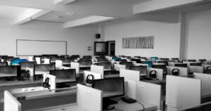 Ufficio open space con file di scrivanie e computer desktop con monitor, tastiere e cuffie