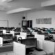 Ufficio open space con file di scrivanie e computer desktop con monitor, tastiere e cuffie