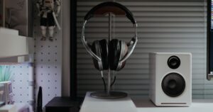 Cuffie over-ear appese a un supporto sulla scrivania accanto a una cassa acustica bianca e al bordo di un monitor